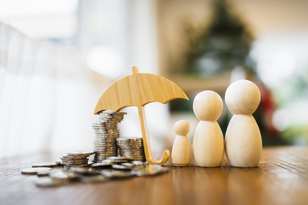 Wood umbrella over stack of coins next to wooden family. Security and protection with life insurance.