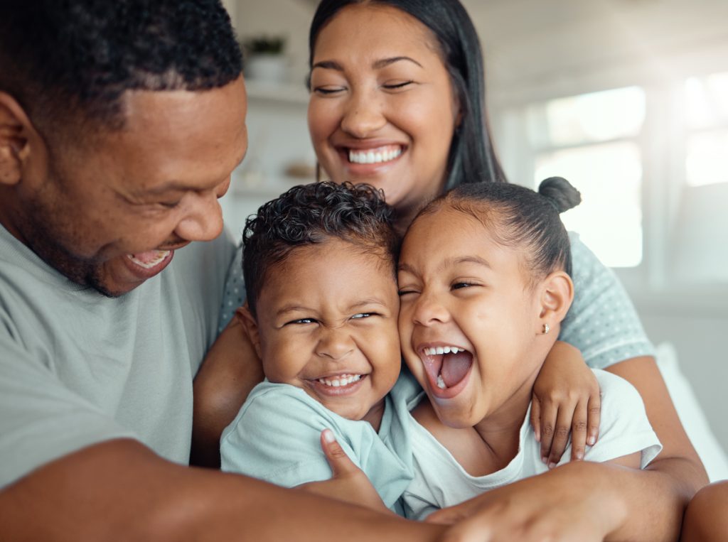 Parents and two kids smiling and hugging because they have life insurance.